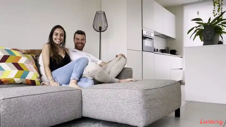 Una coppia sorridente seduta su un divano, immagine della piattaforma Lustery